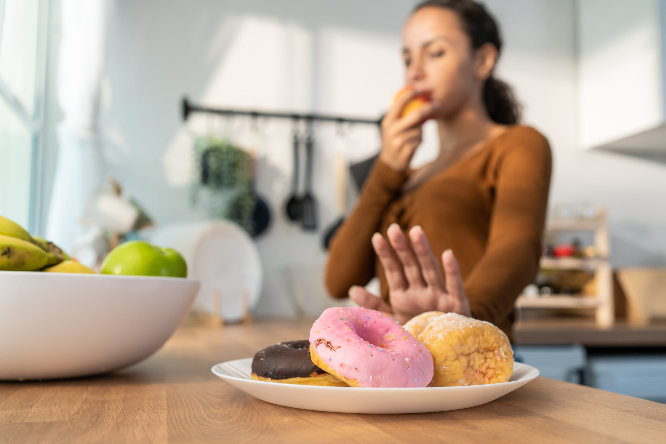 Woman choosing fruit over sugary donuts in kitchen to protect teeth from sugar-related tooth decay