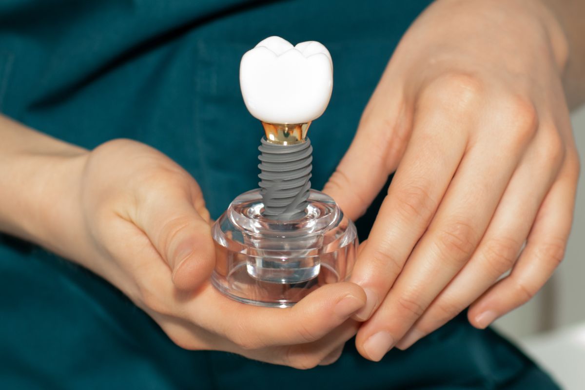 Dental professional holding a model of a dental implant with crown to demonstrate tooth replacement procedure