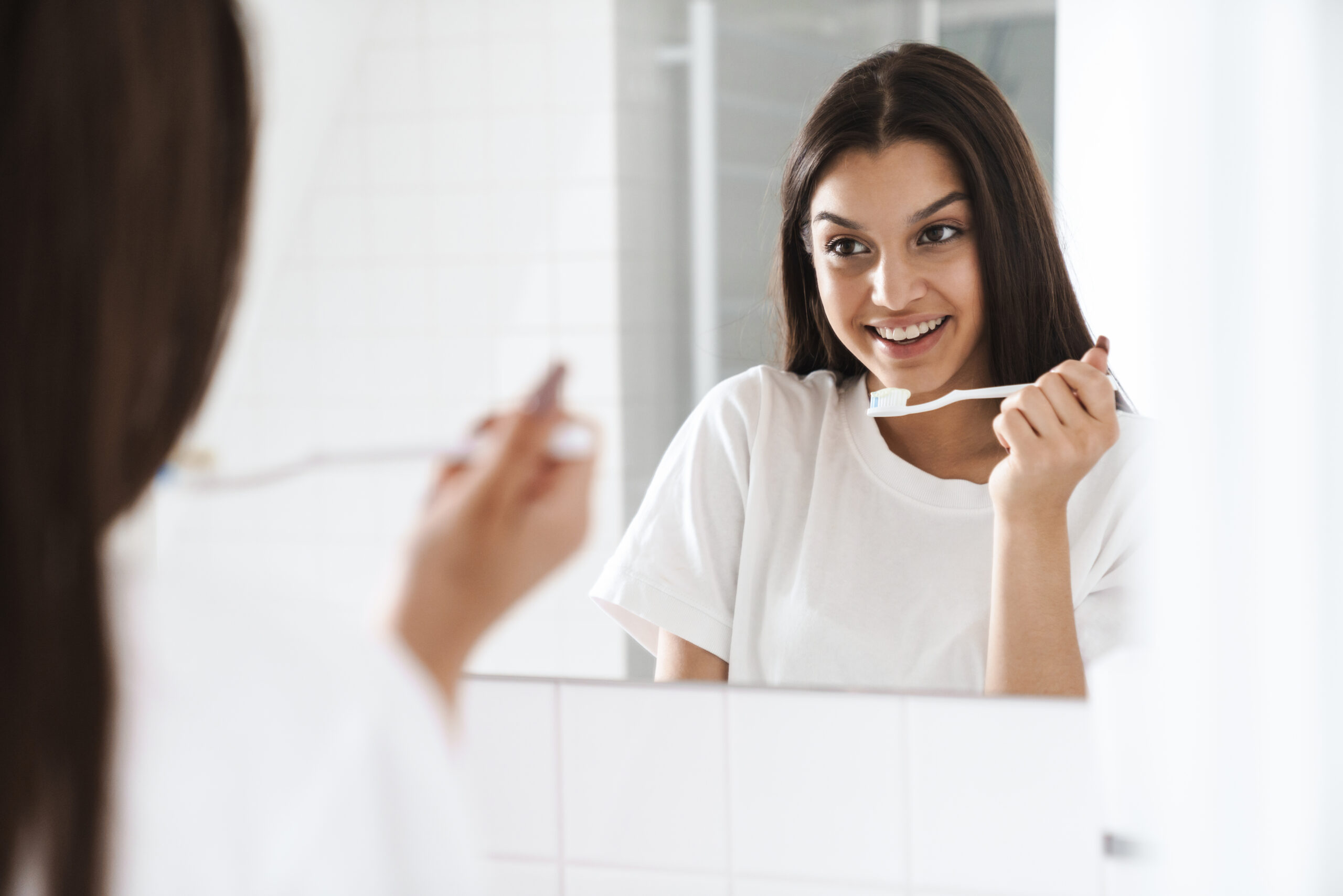 Woman brushing her teeth in front of a mirror, demonstrating a healthy daily oral care routine at home